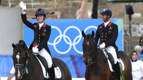 Charlotte Dujardin and Carl Hester on their horses in full outfits wave to the crowd at the Oympics