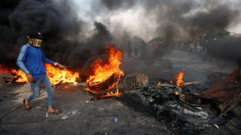 A demonstrator wearing a mask and walking above burning tyres in Basra, southern Iraq