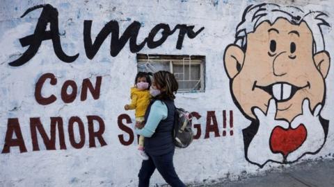 woman carrying her baby walk past a mural promoting the April 10 recall referendum on the presidency of Mexican President Andres Manuel Lopez Obrador, in Mexico City, Mexico March 31, 2022.