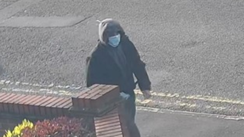 A man wearing black puffer jacket, jogging bottoms, a Covid mask and blue latex gloves