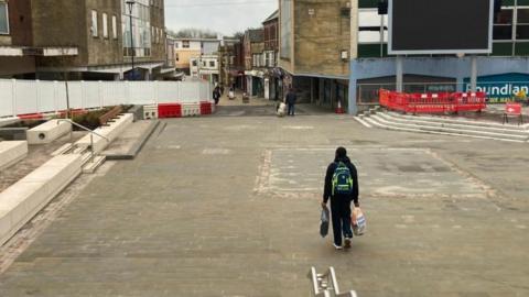 The Triangle square in Yeovil, which has fencing around the edge and a person walking through the middle.