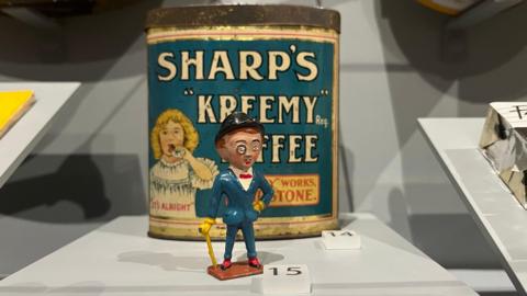 A miniature tin figure of Sir Kreemy Knut, wearing a blue suit with monocle and walking cane, on display in The Oldham Gallery at Maidstone Museum