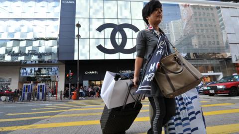 A Mainland Chinese tourist crosses the street carrying multiple shopping bags in the Tsim Sha Tsui region of Hong Kong.