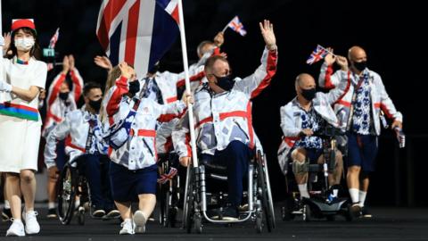 Ellie Simmonds and John Stubbs carry the Great Britain flag, with other members of the ParalympicsGB team following them