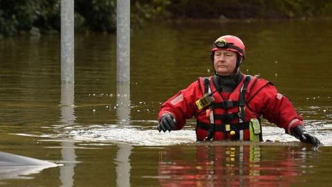 A member of the Fire and Rescue service wades through flood water