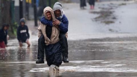 A man carries an elderly man across a flooded road during heavy flooding as a result of a storm in Sir Lowry's Village, close Somerset West on September 25, 2023.