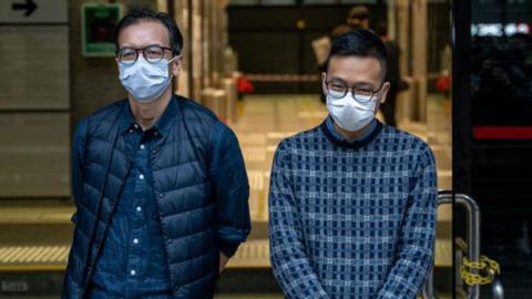 Chung Pui-kuen and Patrick Lam posing for a photo in front of the Wan Chai District Court. They are both wearing glasses and face masks. Patrick Lam appears to be smiling slightly.