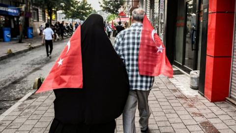 Two people walking carrying Turkish flags