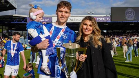 Portsmouth defender Sean Raggett poses with the League One trophy on the pitch with his family