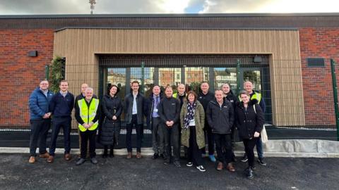 Warden Construction handing the keys over to Blackpool Council and Blackpool Boys and Girls Club outside the new youth centre, a large single storey red brick building with a wood framed glass entrance