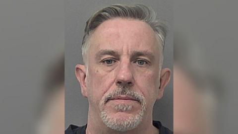 A police head and shoulder's photo of David Young, who has short grey hair and a short grey moustache and beard. He is looking into the camera with a serious expression.
