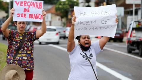 Two protesters carry signs "Ashamed of being white" and "Please stop killing us" outside a Carrefour supermarket in Porto Alegre, Brazil, on 20 November 2020