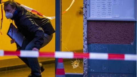 A policeman walks past a hole from a bullet in a window at a crime scene in Berlin's Kreuzberg district on December 26, 2020, following a shooting.