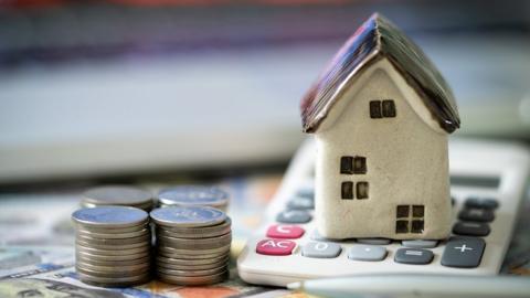 File image of a model house with a pile of coins and banknotes and a calculator