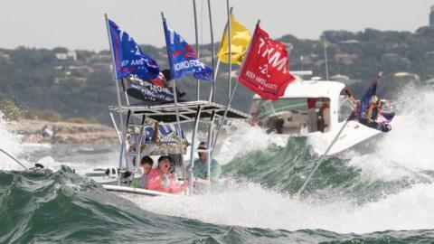 A boat is engulfed in waves from the large wakes of a flotilla of supporters of US President Donald Trump