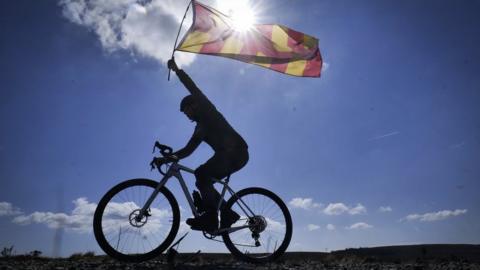 Silhouette of man on bike with sun behind, holding up a flag on a pole