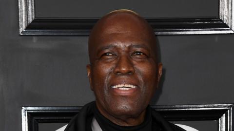 A close-up shot of Albert Mazibuko smiling with a black background behind him