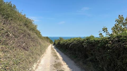 An empty footpath overlooking the sea and under the sunshine