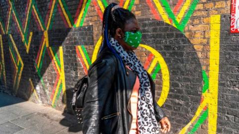 Woman wearing mask walks past mural in London