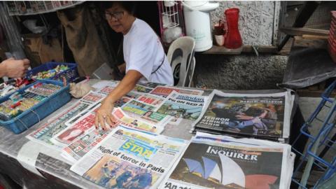 A woman sells newspapers with photos headlines of the Paris attacks in Manila on November 15, 2015