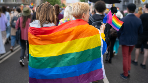 Two people with rainbow Pride flag draped around their shoulders