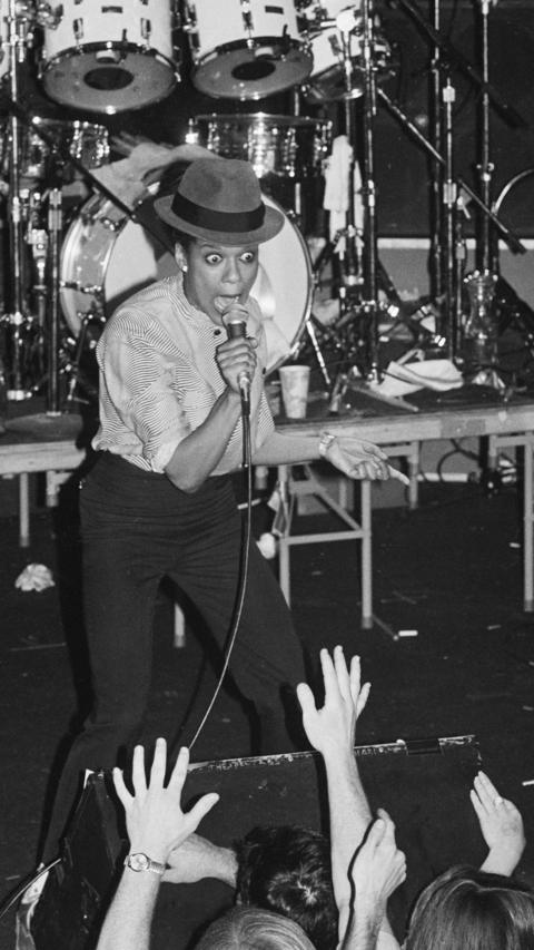 A black and white picture of a woman singing into a microphone on a stage in front of a crowd.