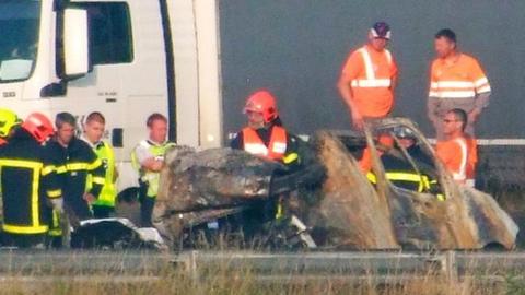 Firefighters and rescuers stand next to the wreckage of a van after it collided with a barricade made with tree trunks set up by migrants on the A16 highway near Guemps, northern France, on 20 June