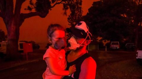 Mike hold his daughter Ella as the skies above turn red during the day on January 4, 2020 in Mallacoota, Australia