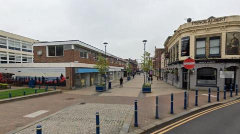 A Google maps image of Biggin Street in Dover. There is a road to the right and pedestrians on the street. 