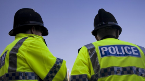 A stock image of two police men facing away from the camera. They are wearing high-vis jackets and wearing black helmets