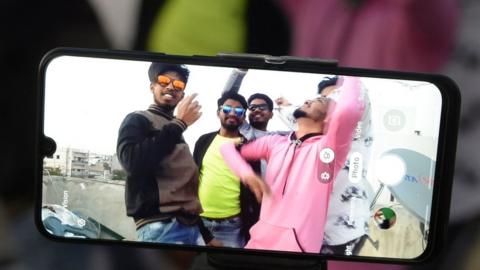 Youths act in front of a mobile phone camera while making a TikTok video on the terrace of their residence in Hyderabad, February 2020