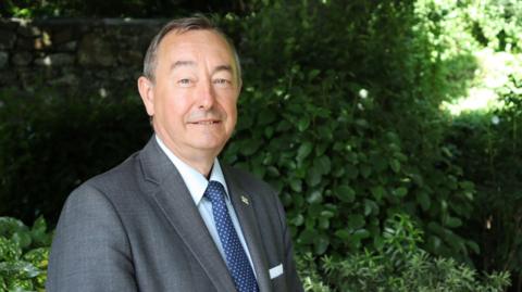 Mark de Garis wearing a suit with a blue tie with plants in the background