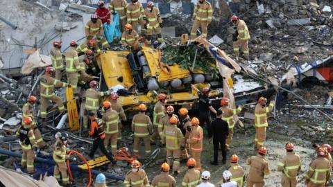 South Korean firefighters search for passengers from a bus trapped by the debris of a collapsed building in Gwangju