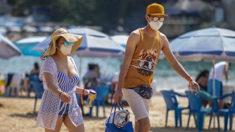 Tourists wearing a mask walk along Caleta beach on March 19 2021 in Acapulco, Mexico