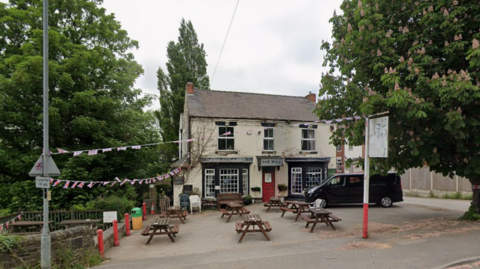 Pub with tables at the front and Union Jack bunting, with a tree to the left