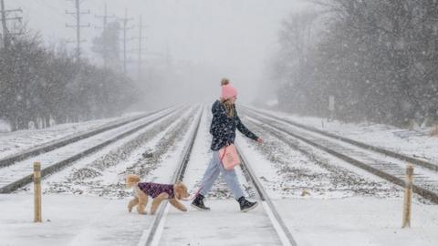 A woman walking her dog crosses train tracks as heavy snowfall begins in a western suburb of Chicago, 22 December 2022