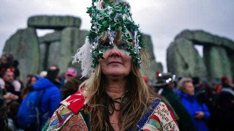 Woman in a light-up headdress in front of Stonehenge