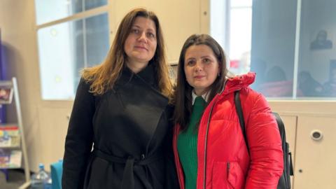 Natalia Sabolik, wearing a black coat, stands next to Ruslana Babee, who is wearing a red coat