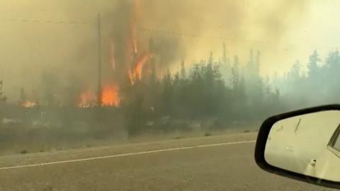 A car surrounded by fire on both sides of the highway