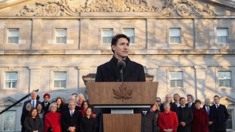 Prime Minister Justin Trudeau at a podium with his new cabinet standing behind him