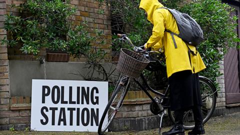A cyclist in a yellow raincoat dismounts outside a polling station in London on 2 May
