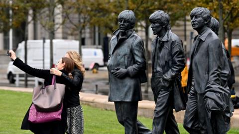 People pose with a statue of members of the Beatles, near the Liver Building in Liverpool, north west England