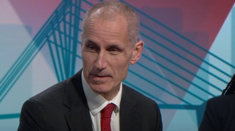 MP Bill Esterson, with close cropped grey hair, a red tie and black suit, speaks in the BBC studio in Salford