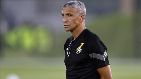 Chris Hughton stands with hands behind his back and looks thoughtful wearing a Ghana top on a training pitch