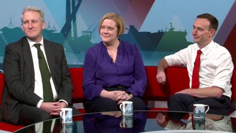 Damian Hinds, wearing a dark suit and green tie, Zoe Franklin wearing a purple blouse and Tom Hayes wearing white shirt with sleeves rolled up on the a red TV studio sofa