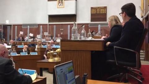 People holding up signs reading "cover up" at an Oldham Council meeting