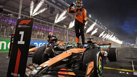 Oscar Piastri stands on his McLaren after winning the Saudi Arabian Grand Prix with fireworks going off in the background