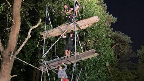 Scaffolders work to try to get the kitten out of the tree