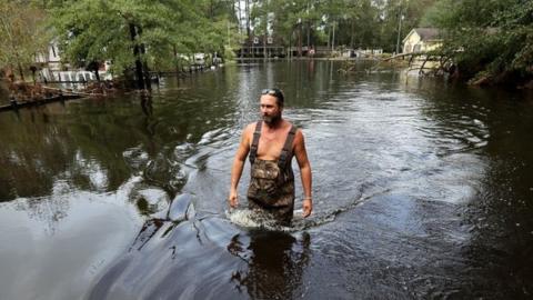 Man wades through thigh-high floodwater in neighbourhood