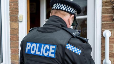 A police officer wearing a blue and black top with Police on it in white writing.